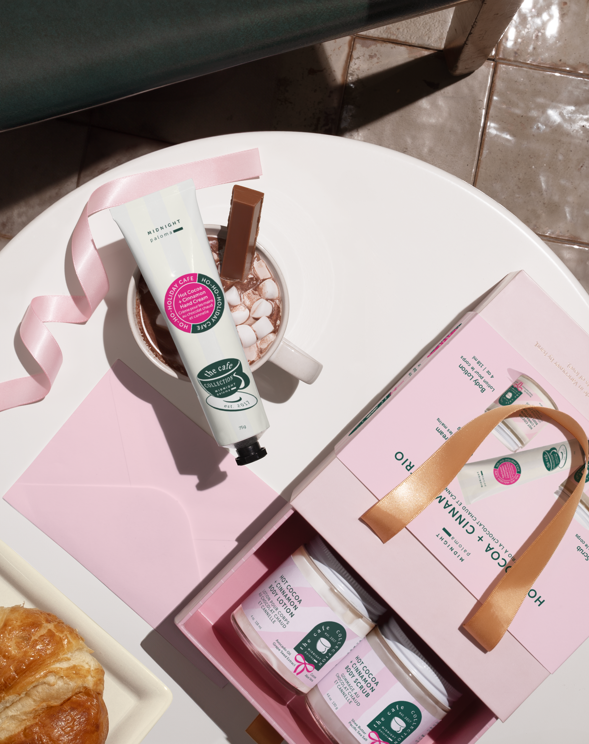 Hand cream and gift box on a pink surface with a croissant